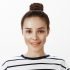 Attractive sensual woman knows how to achieve her goal. Indoor shot of positive good-looking feminine girl with bun hairstyle, smiling flirty while talking with coworker she likes over white wall.